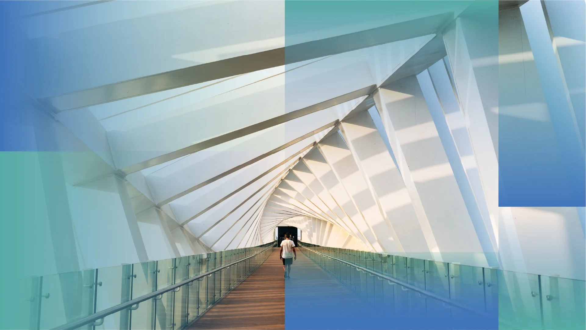 A person walking alone across a long, enclosed pedestrian bridge with white geometric beams and glass railings, illuminated by natural light.